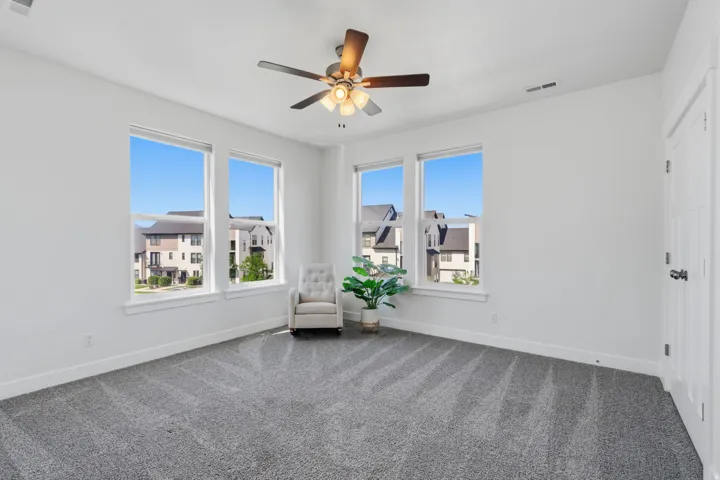 Spacious room featuring multiple large windows, neutral gray carpet, white walls, and a ceiling fan with integrated lighting