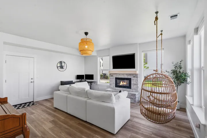 Open-concept living space featuring wood-finish flooring, a contemporary fireplace with a stone surround, and an overhead light fixture