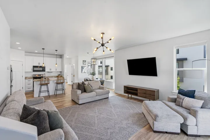 Spacious open-concept living area featuring wood-finish flooring, a modern sputnik chandelier, and expansive windows providing ample natural light
