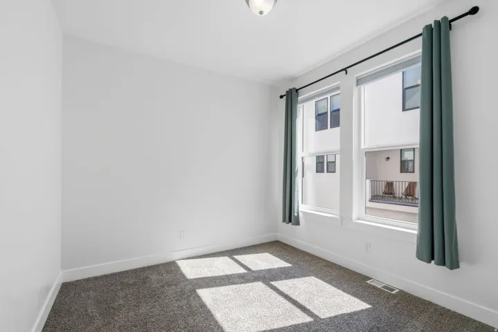 Carpeted room featuring two large windows with roller shades and drapery rods, crisp white walls, and crown molding