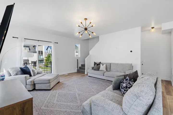 Open-concept living area featuring light wood-finish flooring, a modern sputnik chandelier, and a large sliding glass door with a balcony