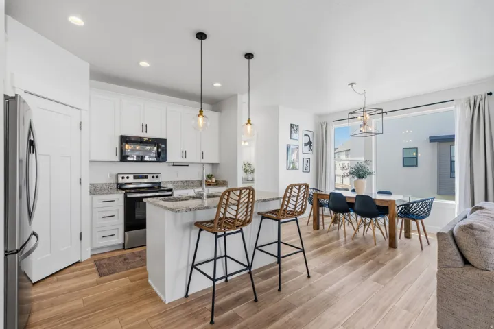 Open-concept living space featuring a kitchen island with pendant lighting, wood-finish flooring, white cabinetry, stainless steel appliances, and a dining area with a large window