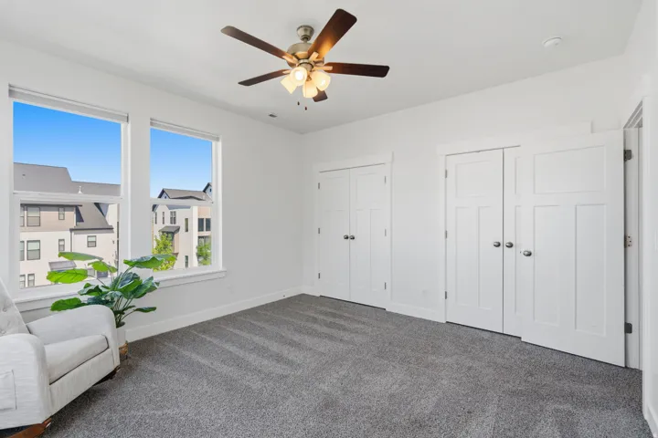 Bright room featuring two large windows, a ceiling fan with integrated lighting, two sets of white double-panel doors, and gray carpeting