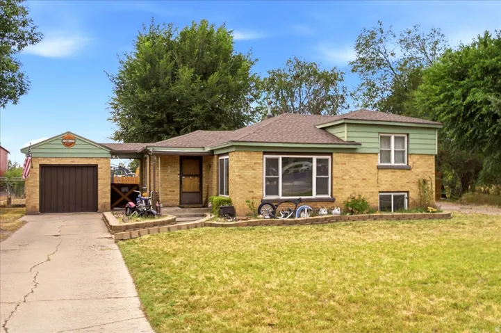 Brick exterior featuring an attached garage with a brown door, a front porch, and a paved driveway