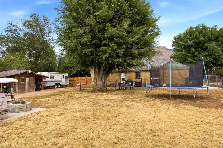 Expansive outdoor space featuring a stone-clad fire pit, mature shade trees, a detached storage shed, and a privacy fence