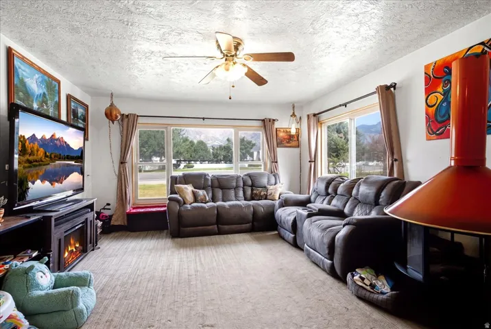 Living area featuring a floor-to-ceiling window, a ceiling fan with integrated lighting, a built-in electric fireplace, and a freestanding red fireplace unit