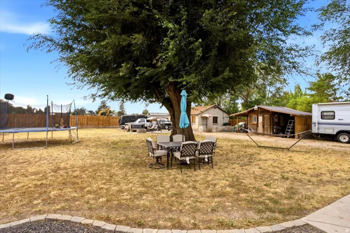 Expansive yard with mature trees, a wooden fence perimeter, and a detached structure