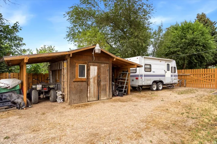 Functional outbuilding with an attached lean-to providing covered storage, a secure wooden gate, and a gravel surface