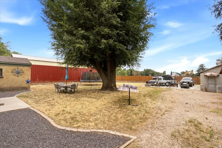 Expansive outdoor area featuring a mature shade tree, gravel pathways, and a red barn structure