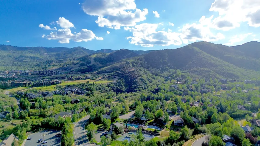 Expansive mountain landscape featuring lush green trees, scattered residential properties, and a winding road