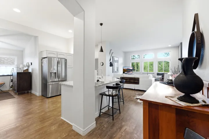 Open-concept living space featuring wood-finish flooring, a kitchen island with seating, stainless steel appliances, and a living area with multiple windows