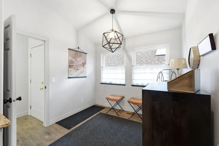 Vaulted ceiling with a geometric pendant light fixture, two windows with white blinds, wood-finish flooring, and a dark wood-finish cabinet
