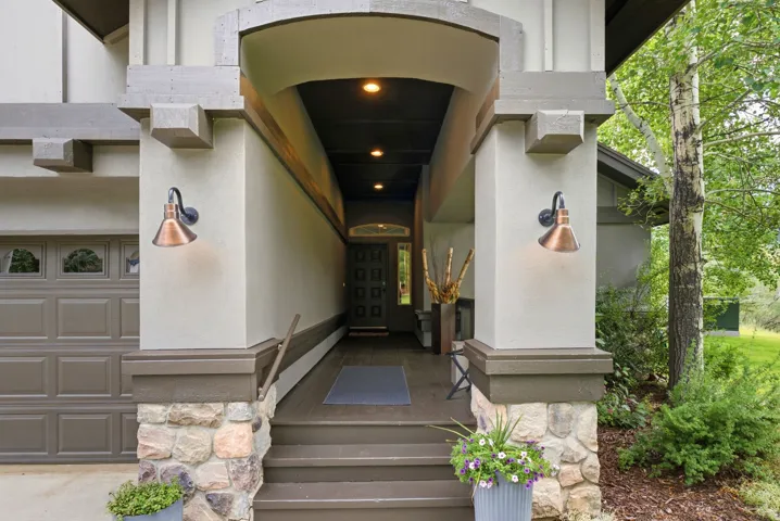 Covered entryway featuring a paneled front door, stone column bases, and two wall-mounted bronze-finish sconces