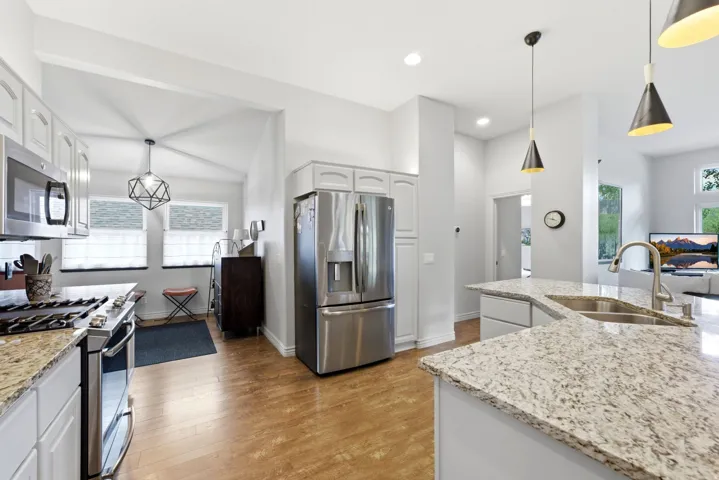 Modern kitchen featuring stainless steel appliances, granite countertops, wood-finish flooring, white cabinetry, and contemporary pendant lighting