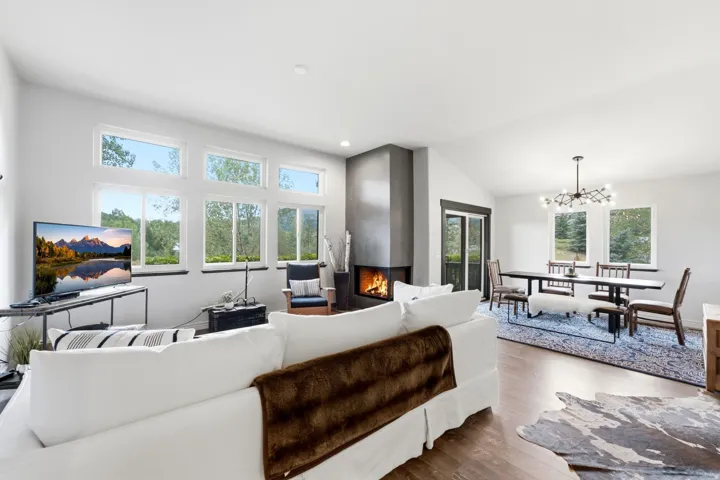Spacious living area featuring a modern fireplace, vaulted ceilings, wood-finish flooring, and multiple windows