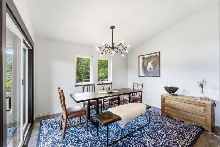 Vaulted ceiling dining area featuring a modern chandelier, wood-finish flooring, and multiple windows
