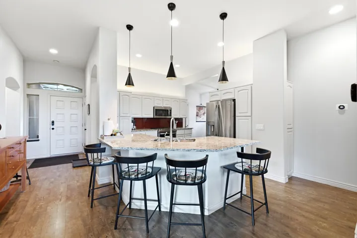 Kitchen with a granite-topped island, white cabinetry, stainless steel appliances, and wood-finish flooring