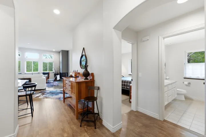 Central hallway with wood-finish flooring, leading to a living area with large windows, a sleek fireplace, and recessed lighting