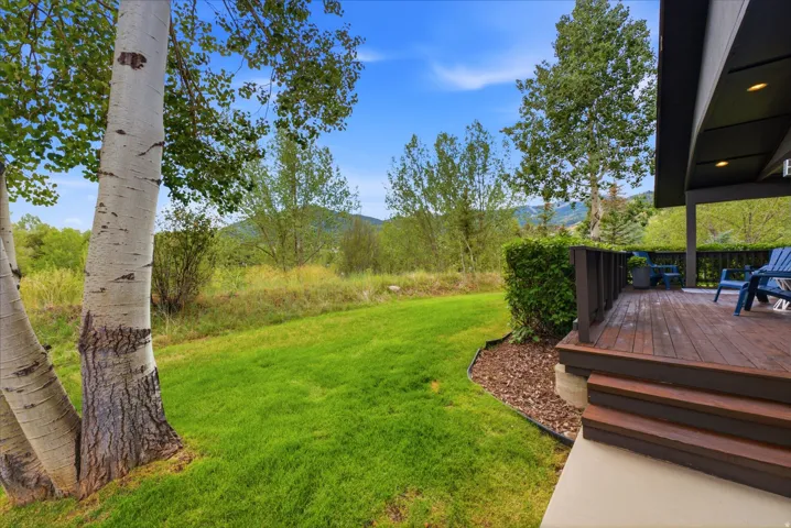 Spacious backyard featuring a manicured lawn, mature trees, and a multi-level wood deck with steps