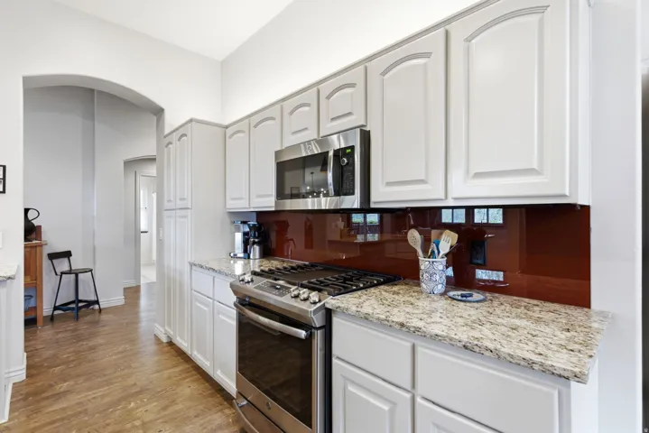 Kitchen featuring light cabinetry, granite countertops, stainless steel gas range, and a coordinating microwave