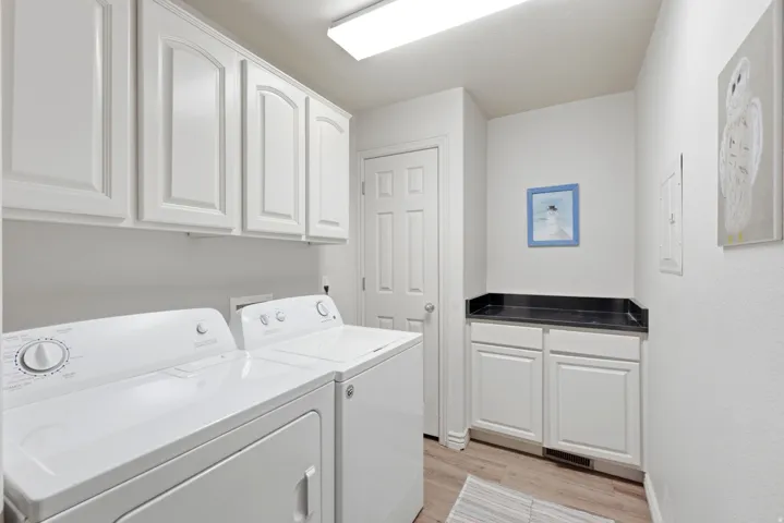 Functional utility room featuring upper white cabinetry, a built-in countertop with dark surfacing, lower white cabinetry, and wood-finish flooring