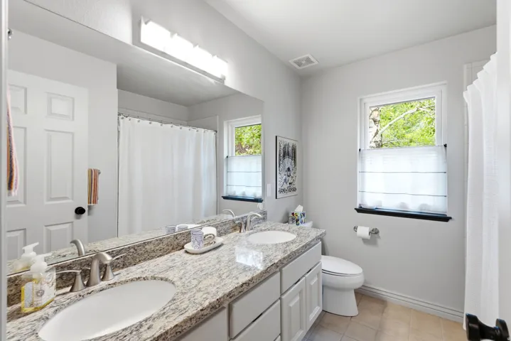 Bathroom featuring dual under-mount sinks with brushed nickel fixtures, a granite-finish countertop, and white shaker-style vanity cabinetry
