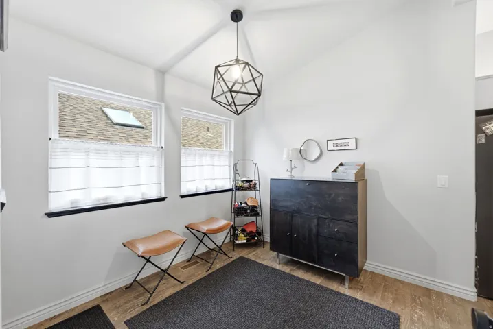 Vaulted ceiling entry featuring two windows with white shades, wood-finish flooring, and a contemporary geometric pendant light fixture