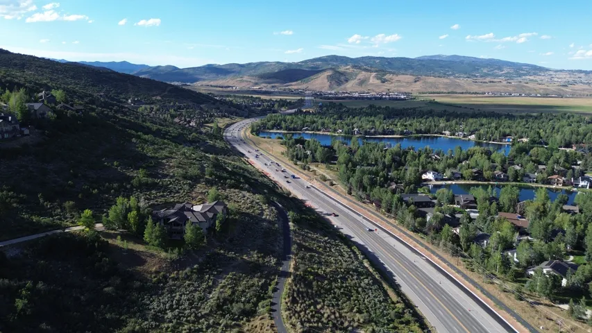 Expansive mountain landscape featuring a multi-lane highway, surrounding hillsides with scattered properties, and a residential area with multiple lakes