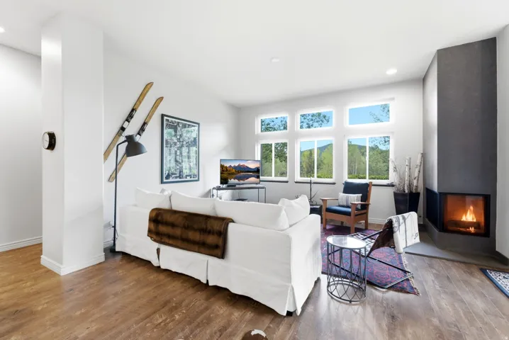 Living area featuring wide plank wood-finish flooring, a contemporary corner fireplace with a dark-toned hearth, and multiple windows with white trim