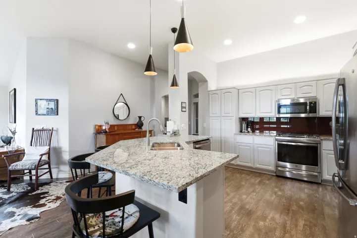 Kitchen featuring an angled granite island with bar seating, pendant lighting, white cabinetry, stainless steel appliances, and wood-finish flooring