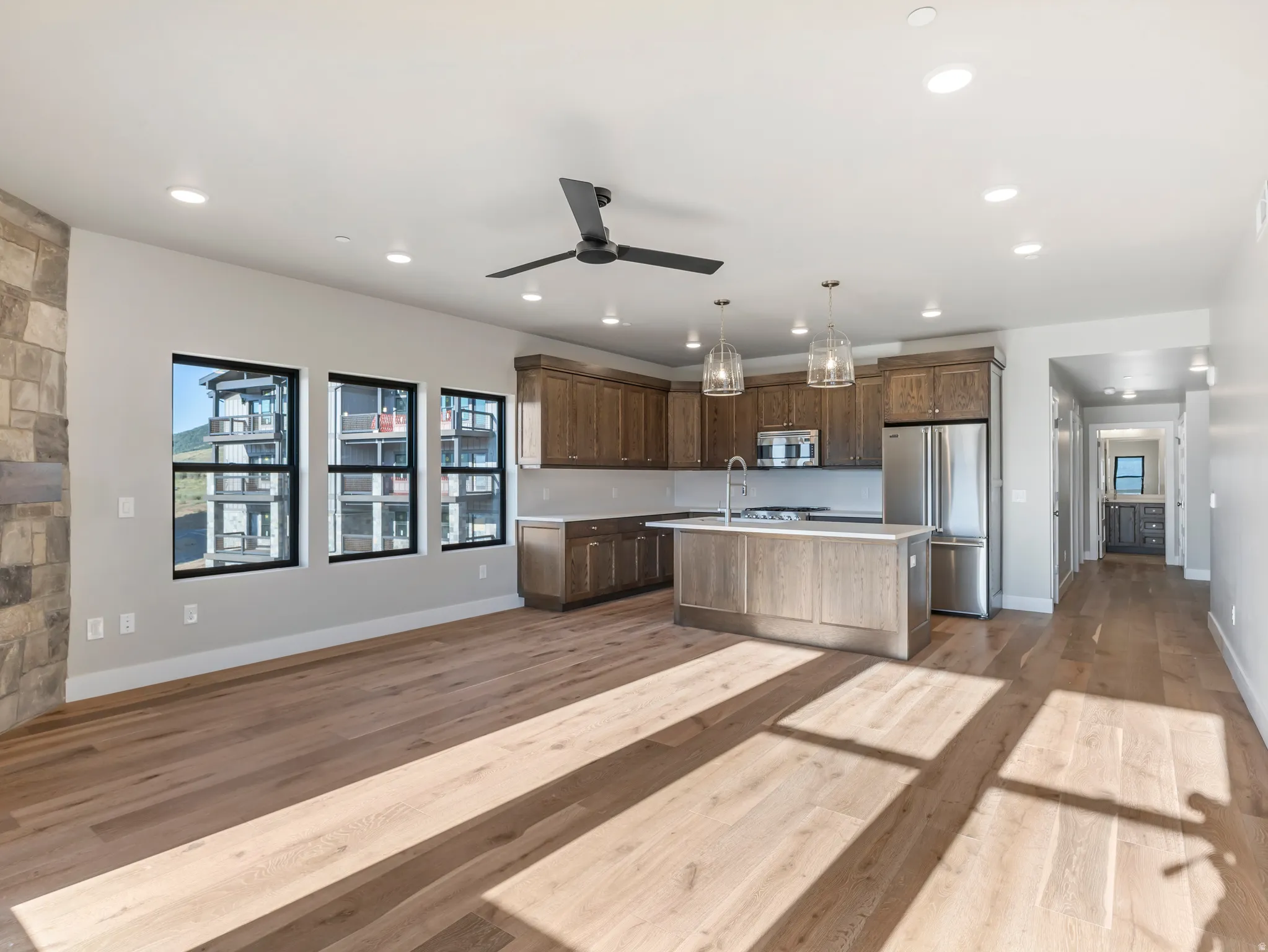 Open-concept living space featuring wood-finish flooring, a modern kitchen island with pendant lighting, stainless steel appliances, and a stone accent wall