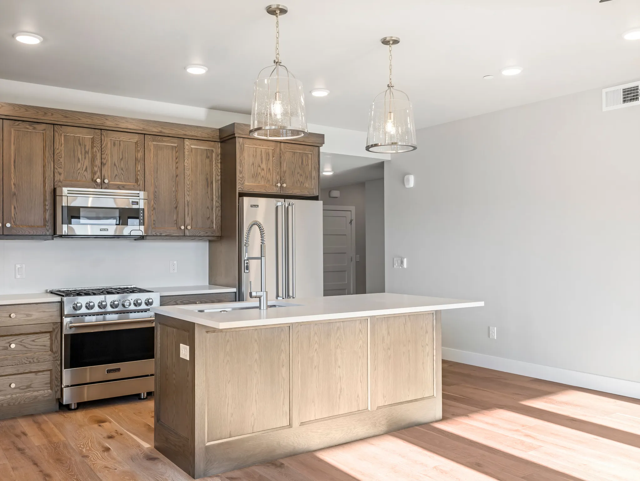 Open-concept kitchen featuring wood-finish cabinetry, stainless steel appliances, a center island with sink, and pendant lighting