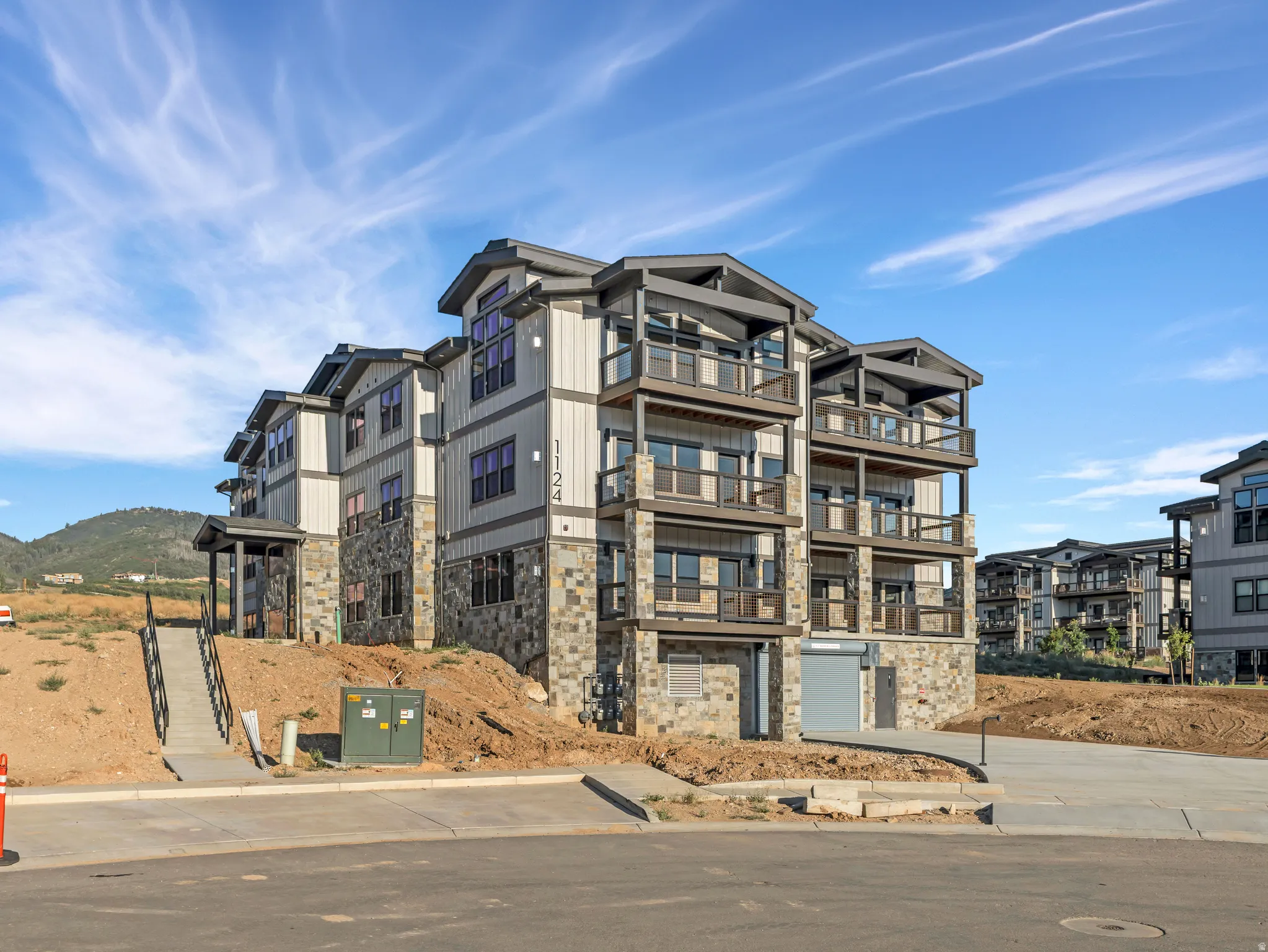 Modern multi-story building featuring stone and siding exterior, multiple private balconies with metal railings, and a prominent entry