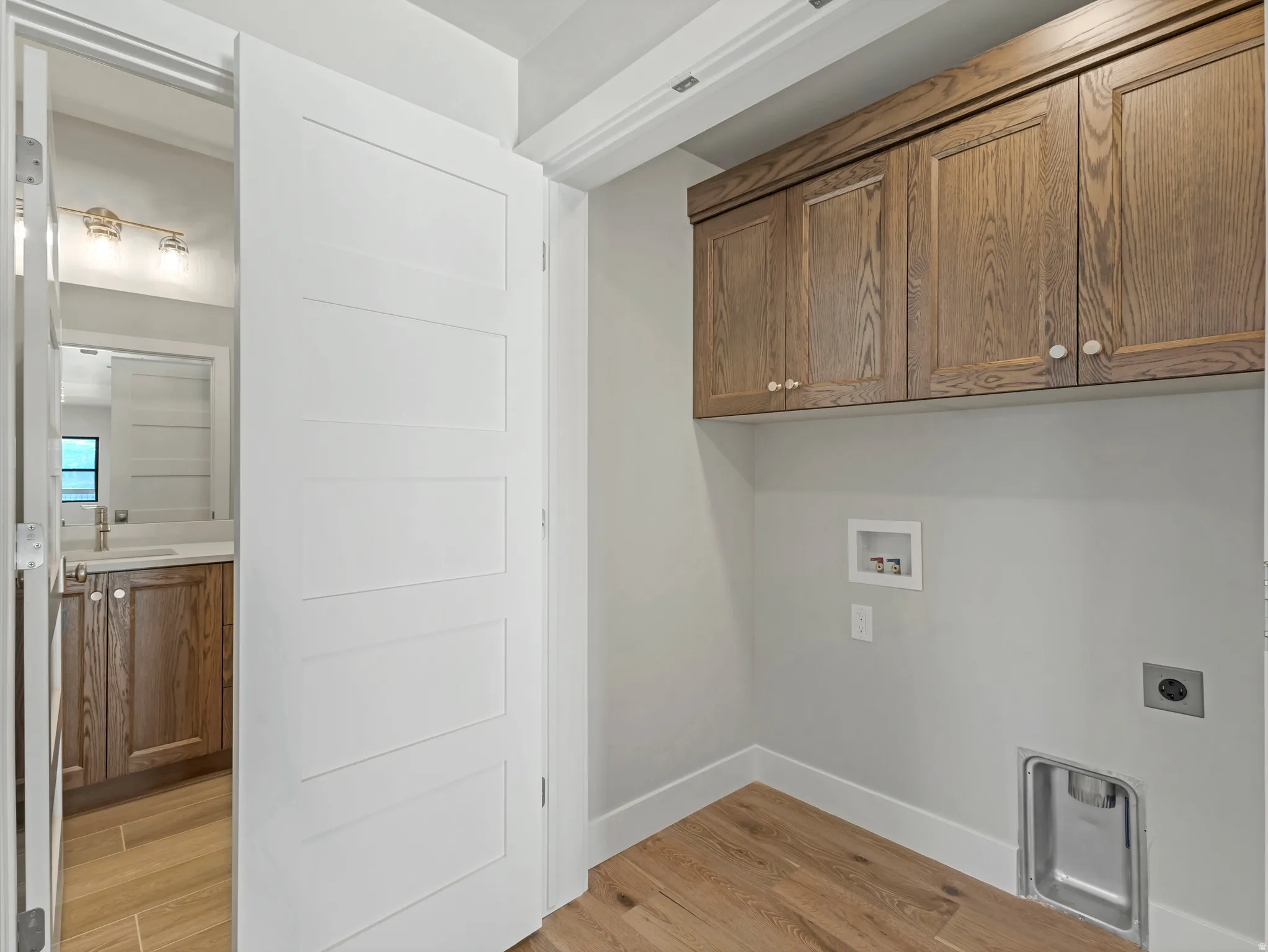 Dedicated laundry area featuring wood-finish flooring and upper wood cabinetry