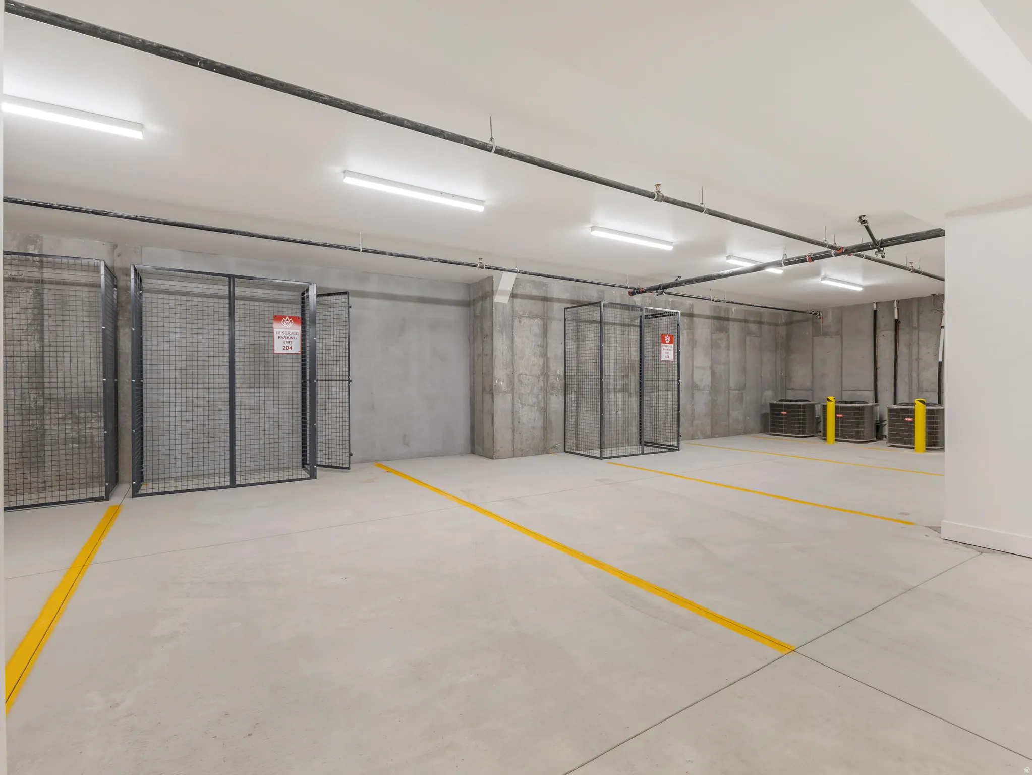 Concrete flooring with yellow demarcation lines, featuring exposed concrete walls and overhead piping