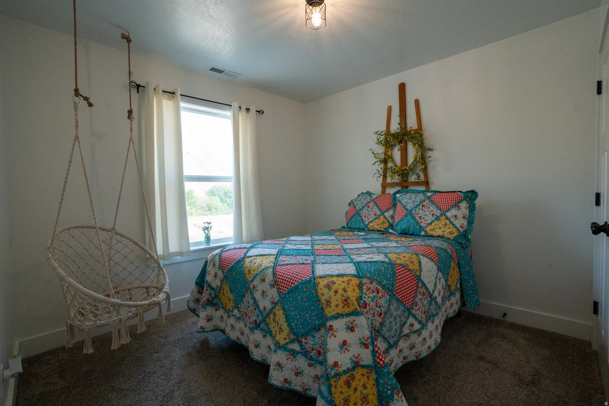 Bedroom featuring neutral wall paint, a single window with white curtains, and carpet flooring