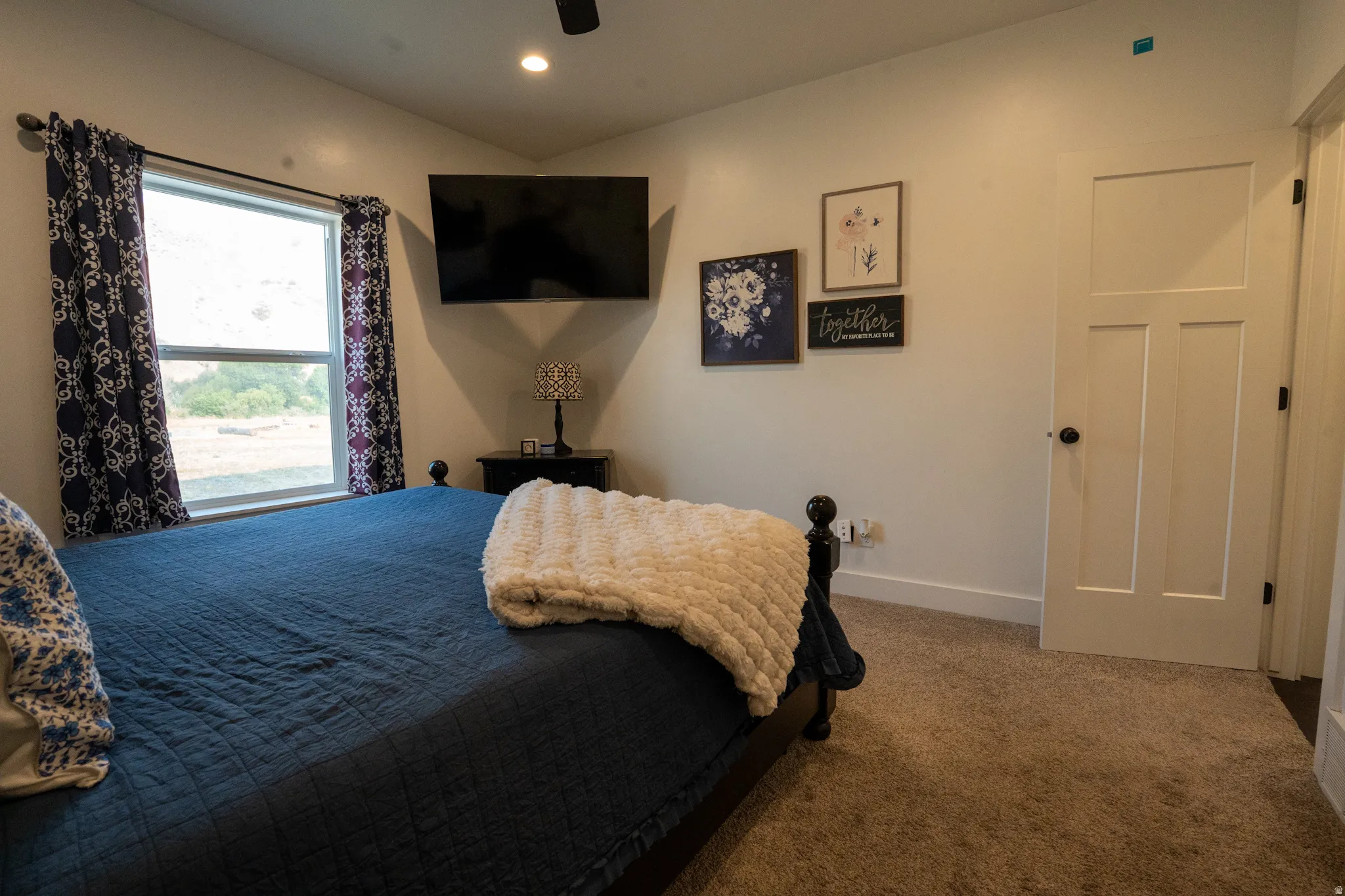 Bedroom featuring carpeted flooring and a window with dark patterned drapes