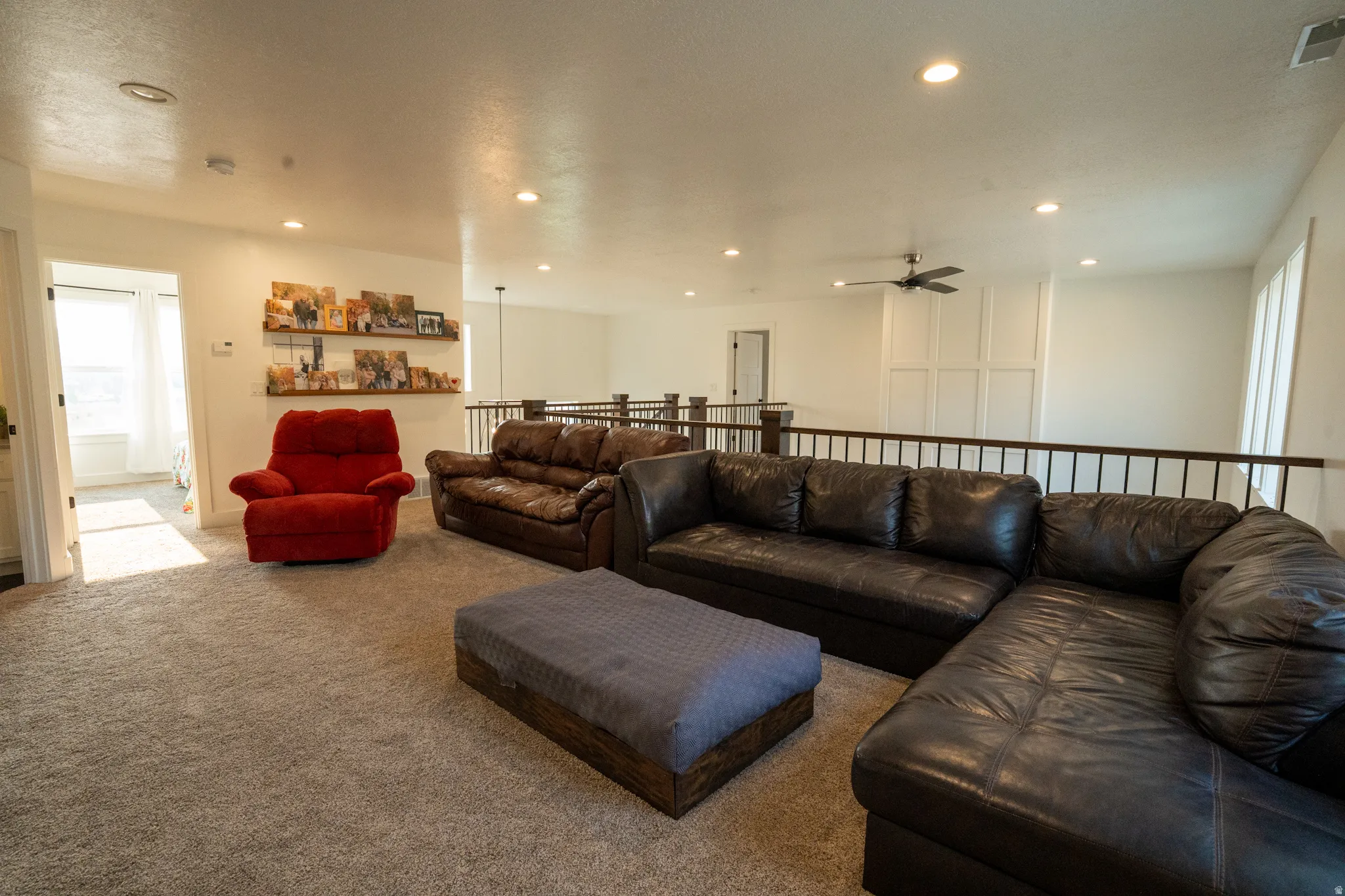 Expansive carpeted loft space featuring recessed lighting, a ceiling fan, and a dark wood and wrought iron railing