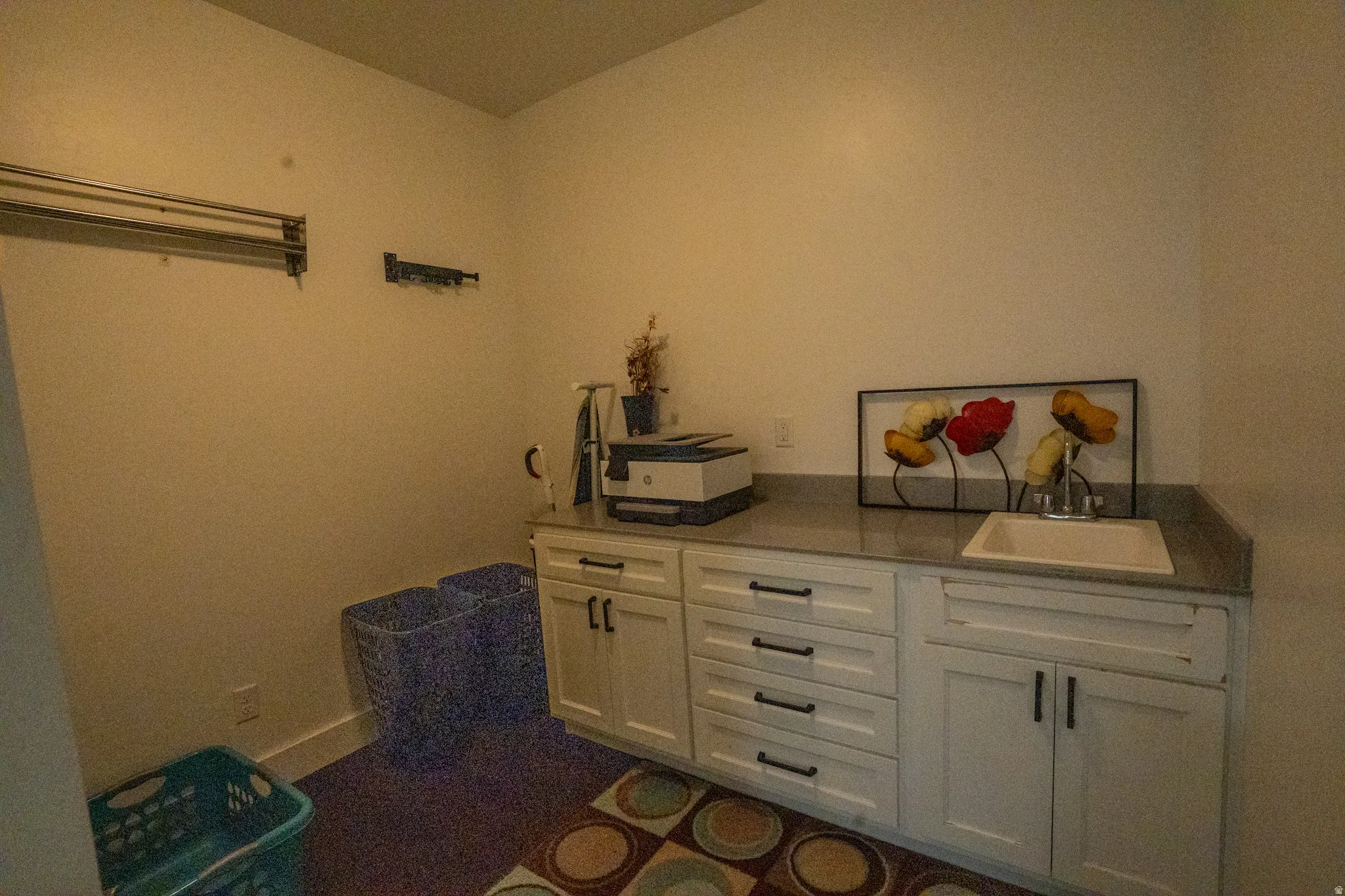 Utility room featuring white cabinetry with multiple drawers and cabinet storage, dark countertop work surface, and patterned area rug flooring