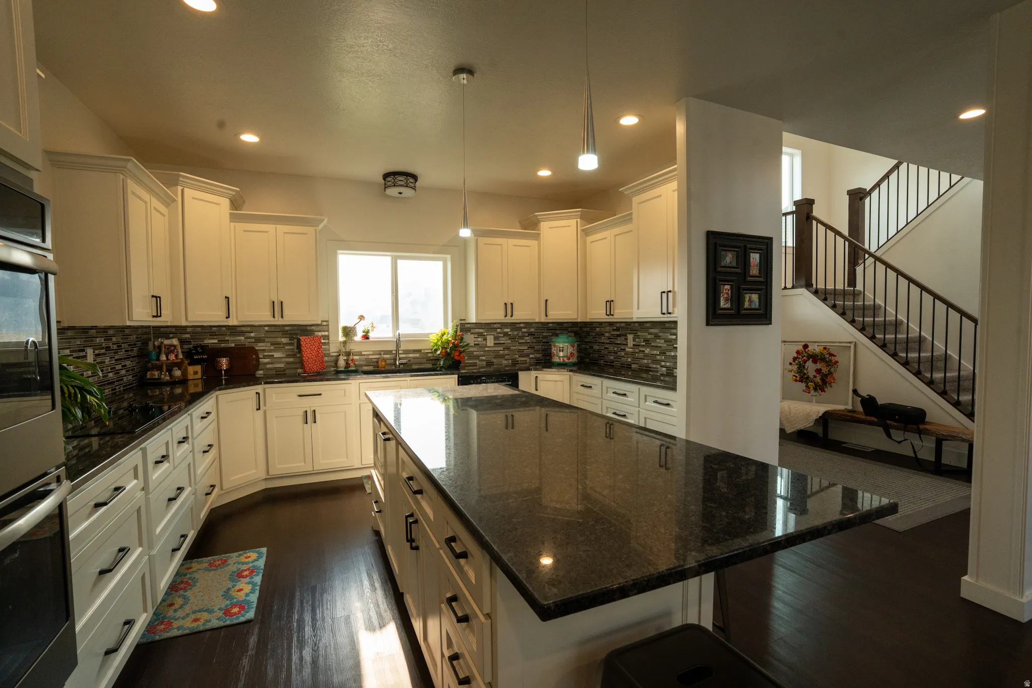 Spacious kitchen featuring an expansive island with a dark countertop, white cabinetry with dark hardware, a mosaic tile backsplash, and stainless steel built-in appliances