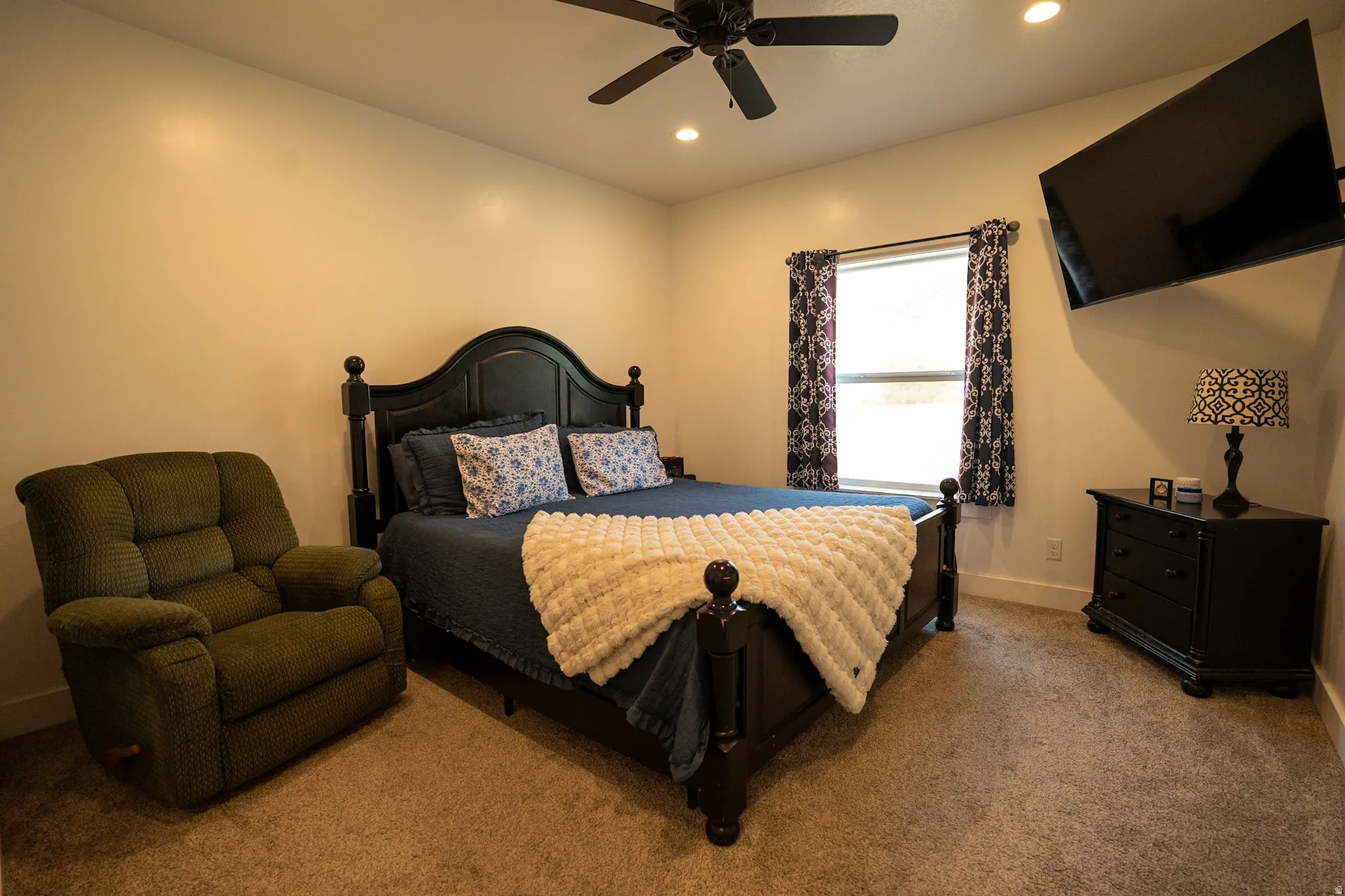 Spacious bedroom featuring a black metal bed frame, warm neutral walls, and ceiling fan with recessed lighting