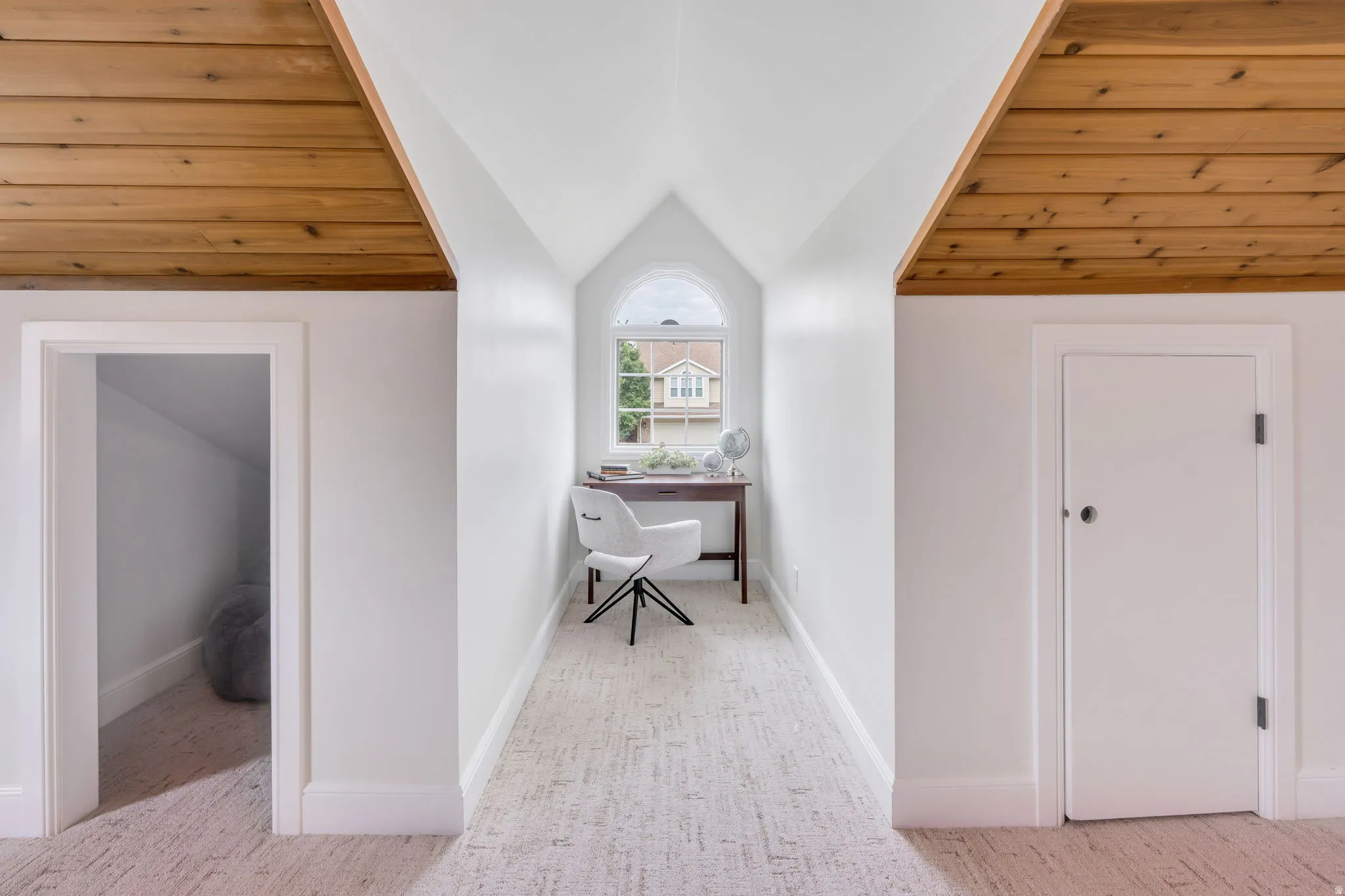 Attic space featuring wood-finish ceiling panels, light-colored carpeting, a built-in arched window, and two recessed doorways