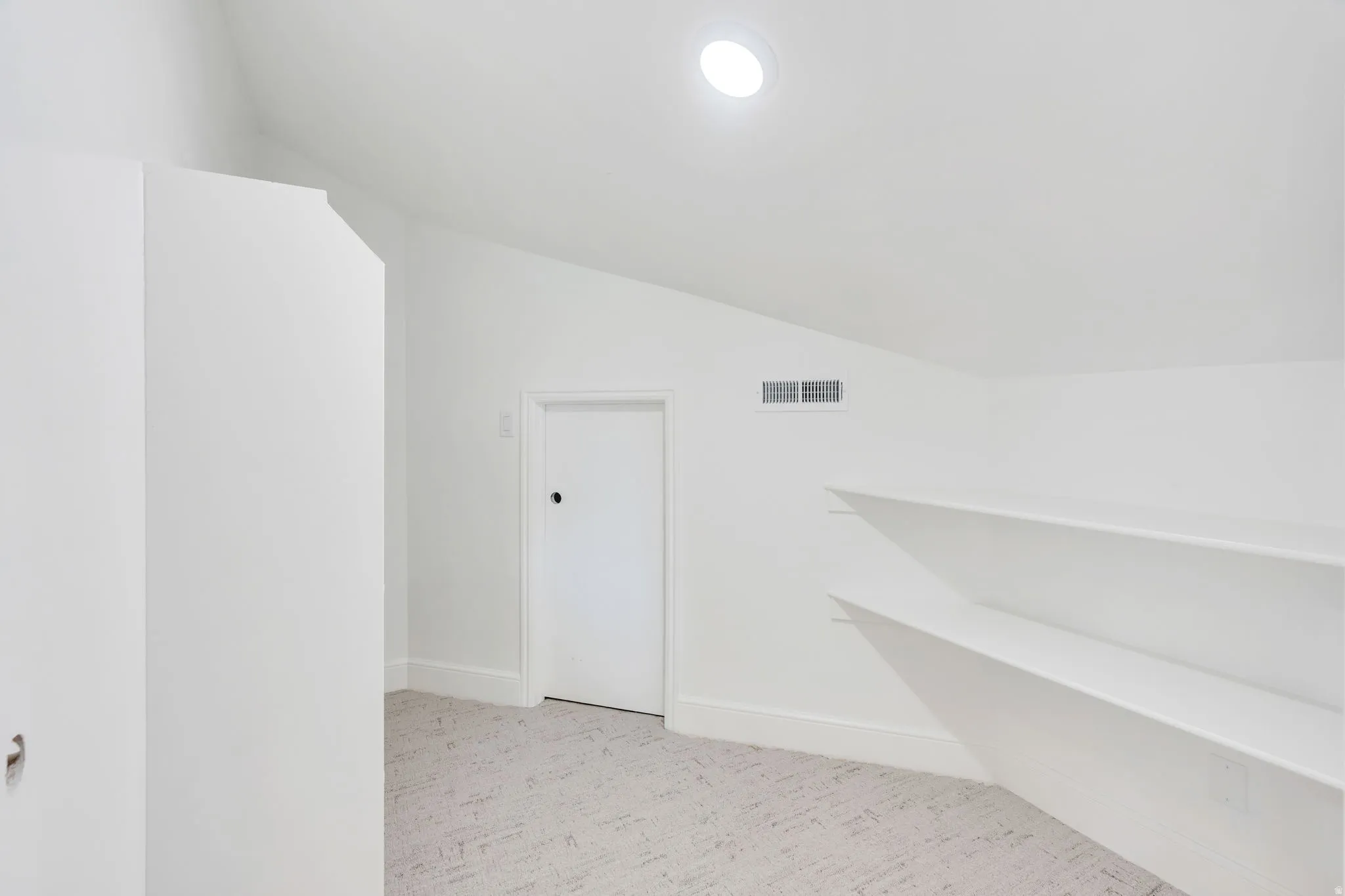 Attic space with sloped ceilings, recessed lighting, wall-mounted shelving, and light-toned patterned carpeting