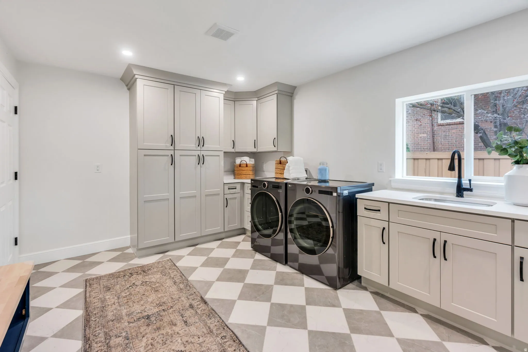 Laundry room featuring checkerboard tile flooring, extensive light gray cabinetry, a built-in sink with a black gooseneck faucet, and white countertops