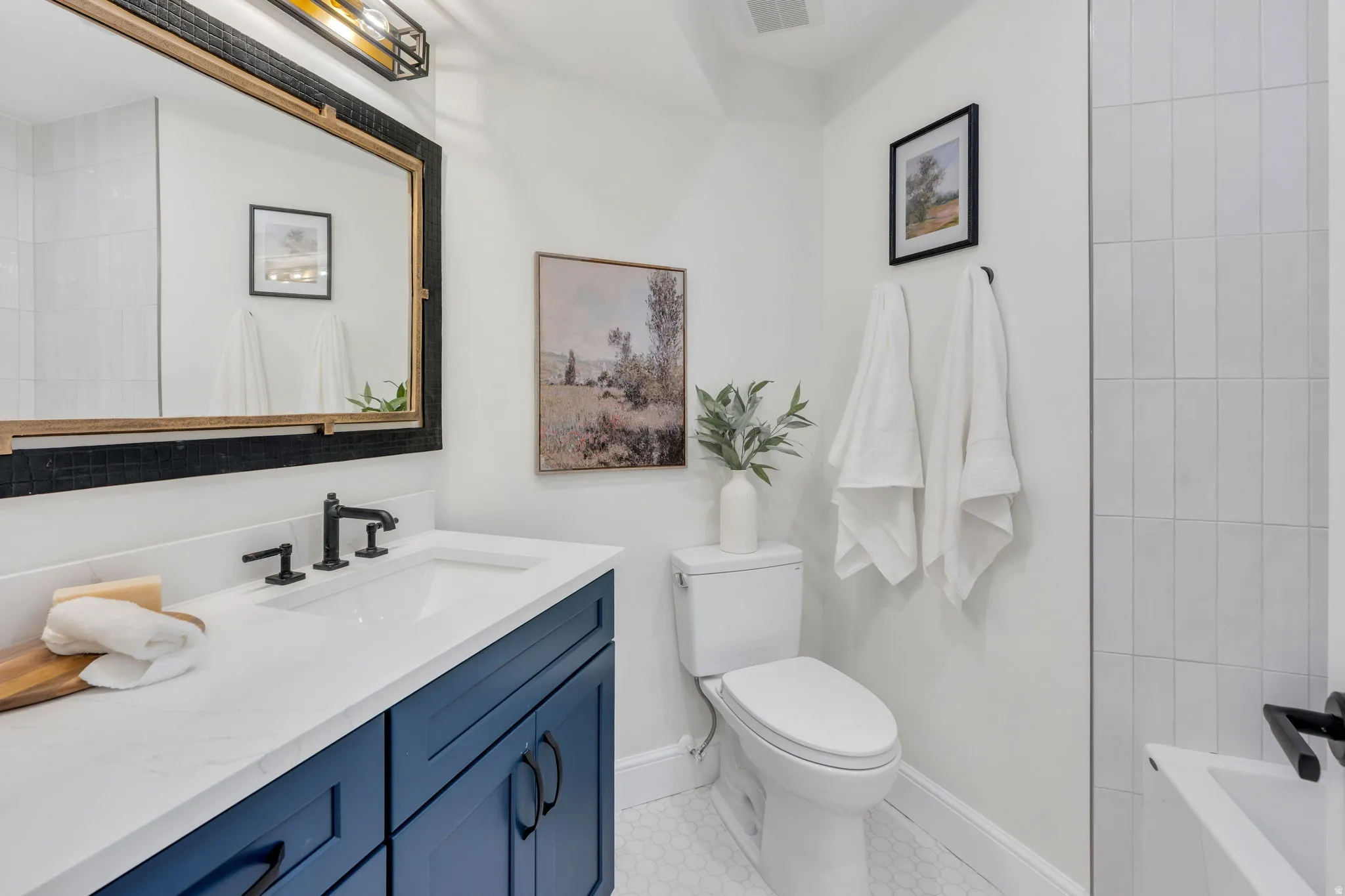 Bathroom featuring a navy blue vanity with a white countertop and rectangular sink, matte black faucet, framed mirror, and hexagonal floor tiling