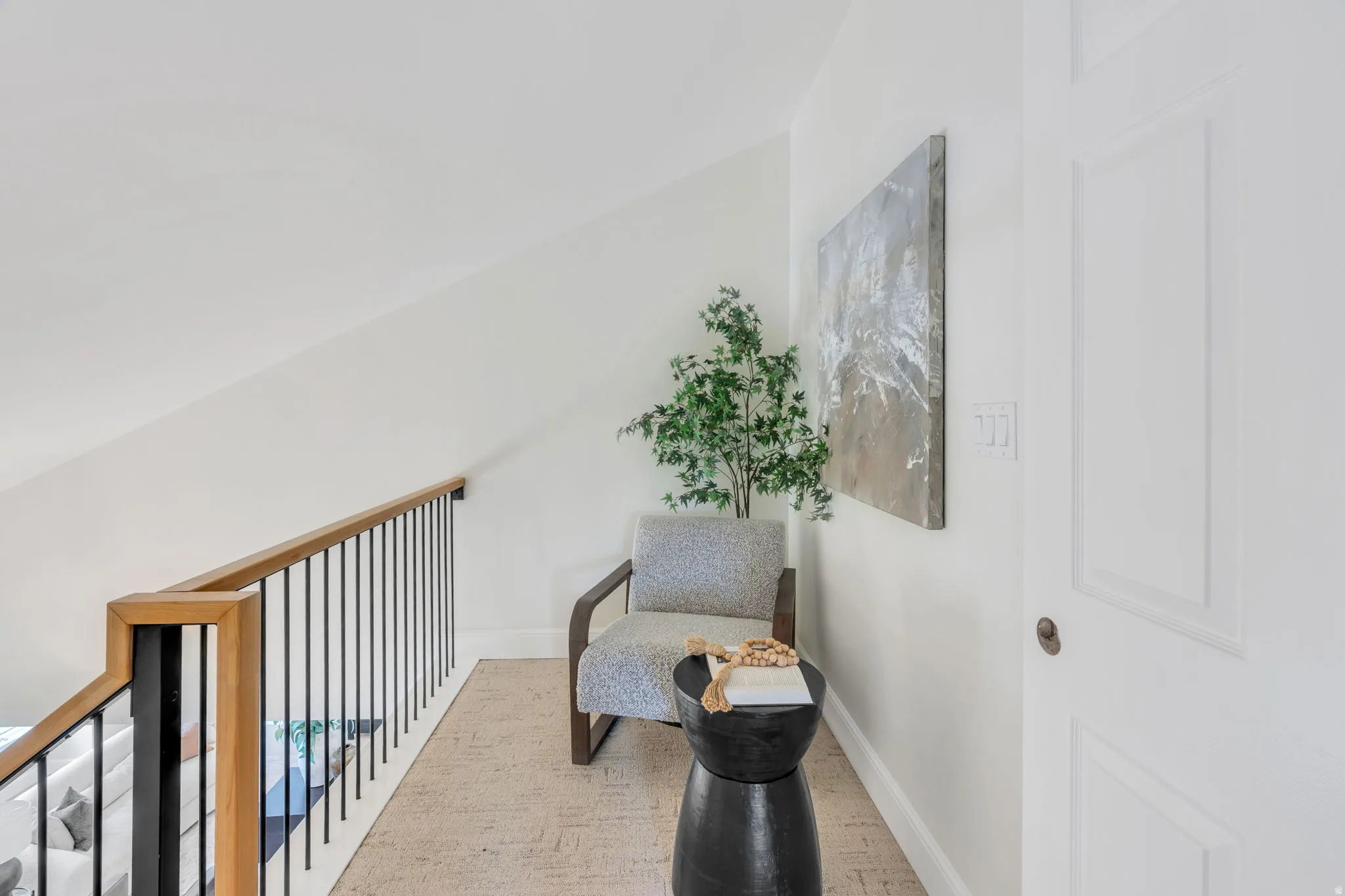 Upper landing area featuring a wood-finish handrail with black metal balusters, light-colored textured carpeting, and white walls