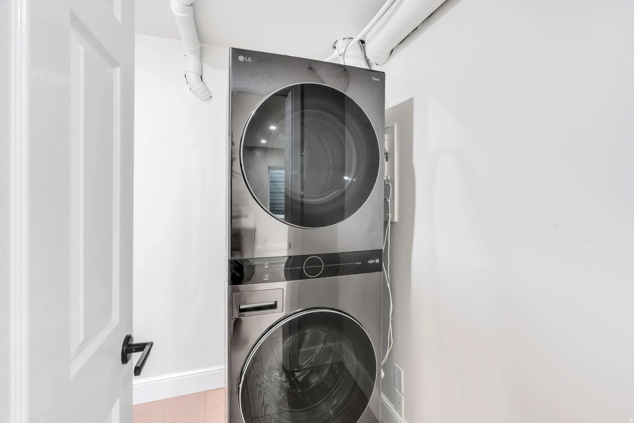 Stackable stainless steel washer and dryer unit with white walls and a white paneled door with black hardware