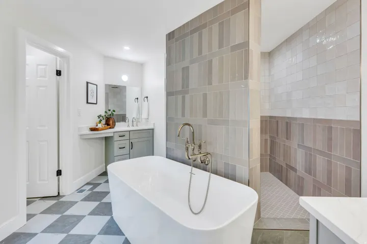 Bathroom featuring a freestanding tub with wall-mounted fixtures, a walk-in shower with vertically stacked subway tile, and a vanity with a white countertop and undermount sink