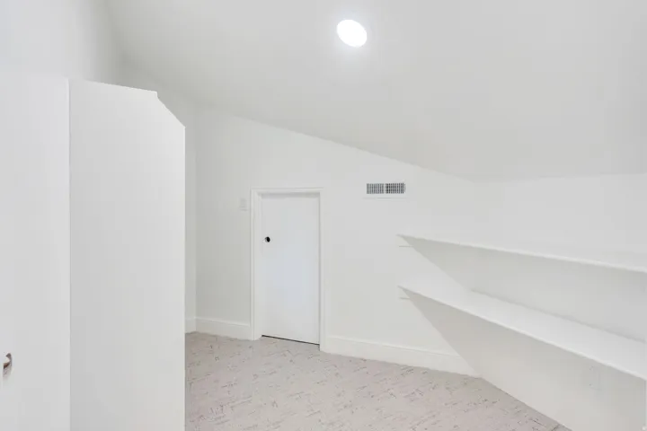 Attic space with sloped ceilings, recessed lighting, wall-mounted shelving, and light-toned patterned carpeting