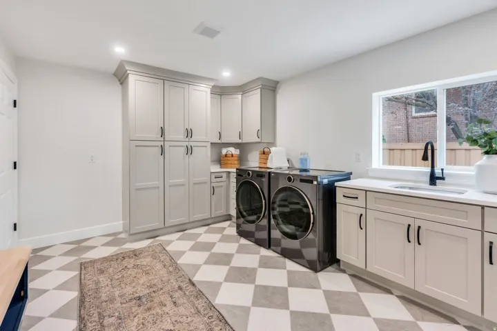 Laundry room featuring checkerboard tile flooring, extensive light gray cabinetry, a built-in sink with a black gooseneck faucet, and white countertops